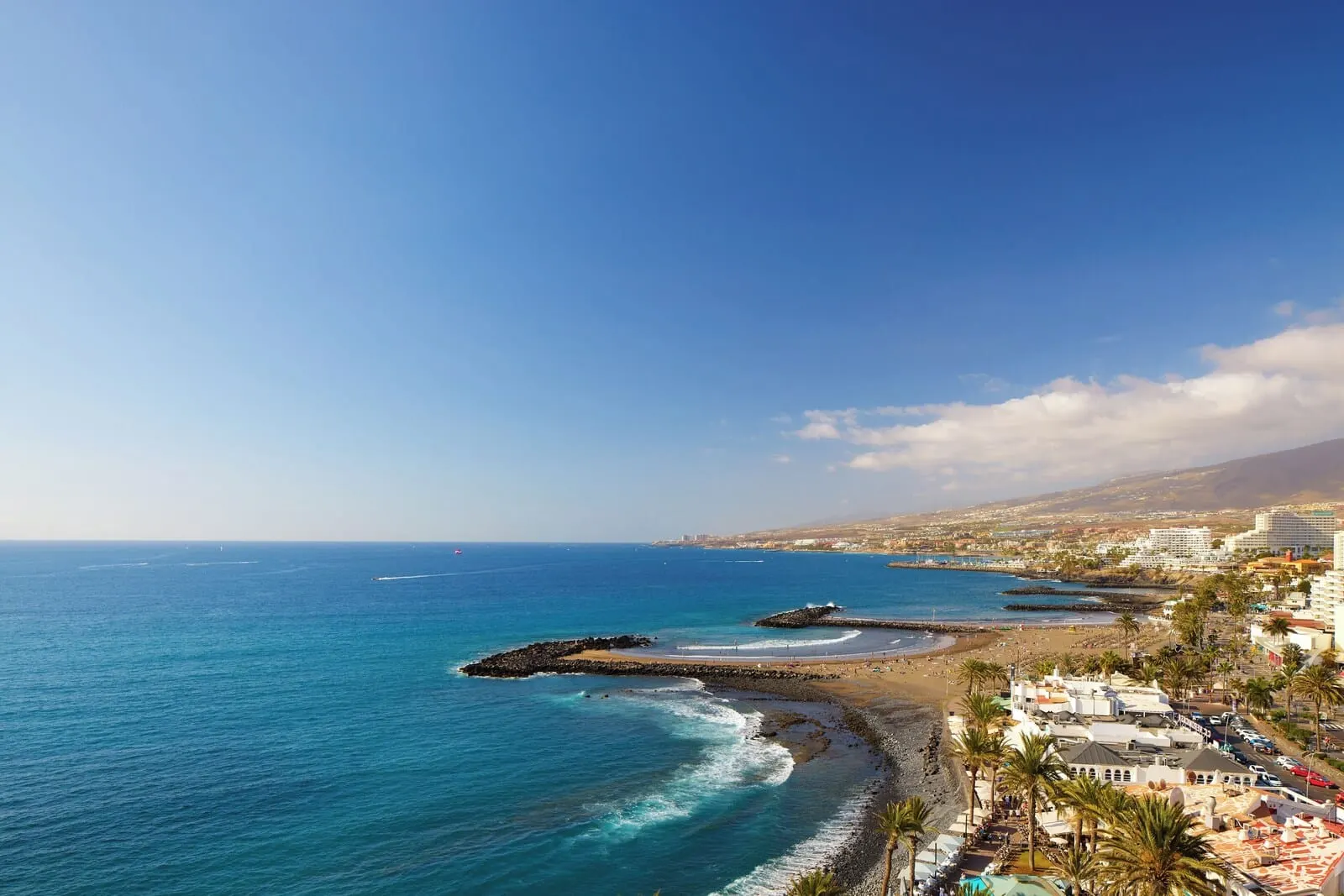 Sol Tenerife: A coastal town with a beach, rocky shoreline, and buildings along the shore