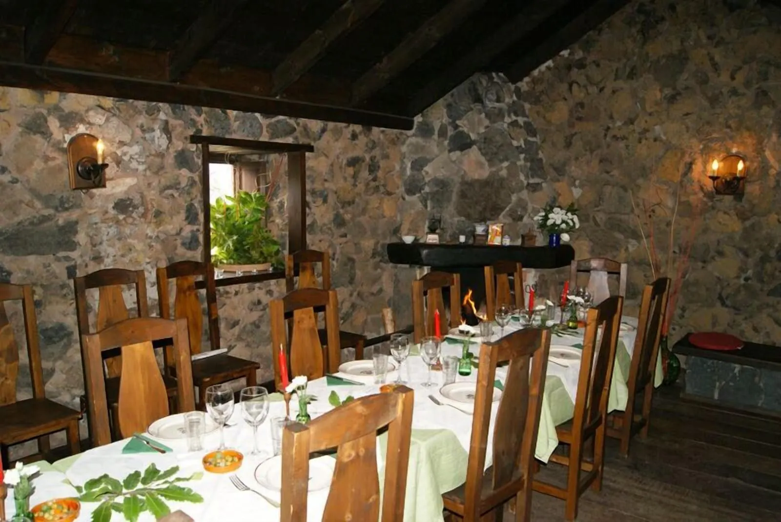 Hotel Rural Caserío Los Partidos: A rustic dining room with stone walls, wooden chairs, and a table set for a meal