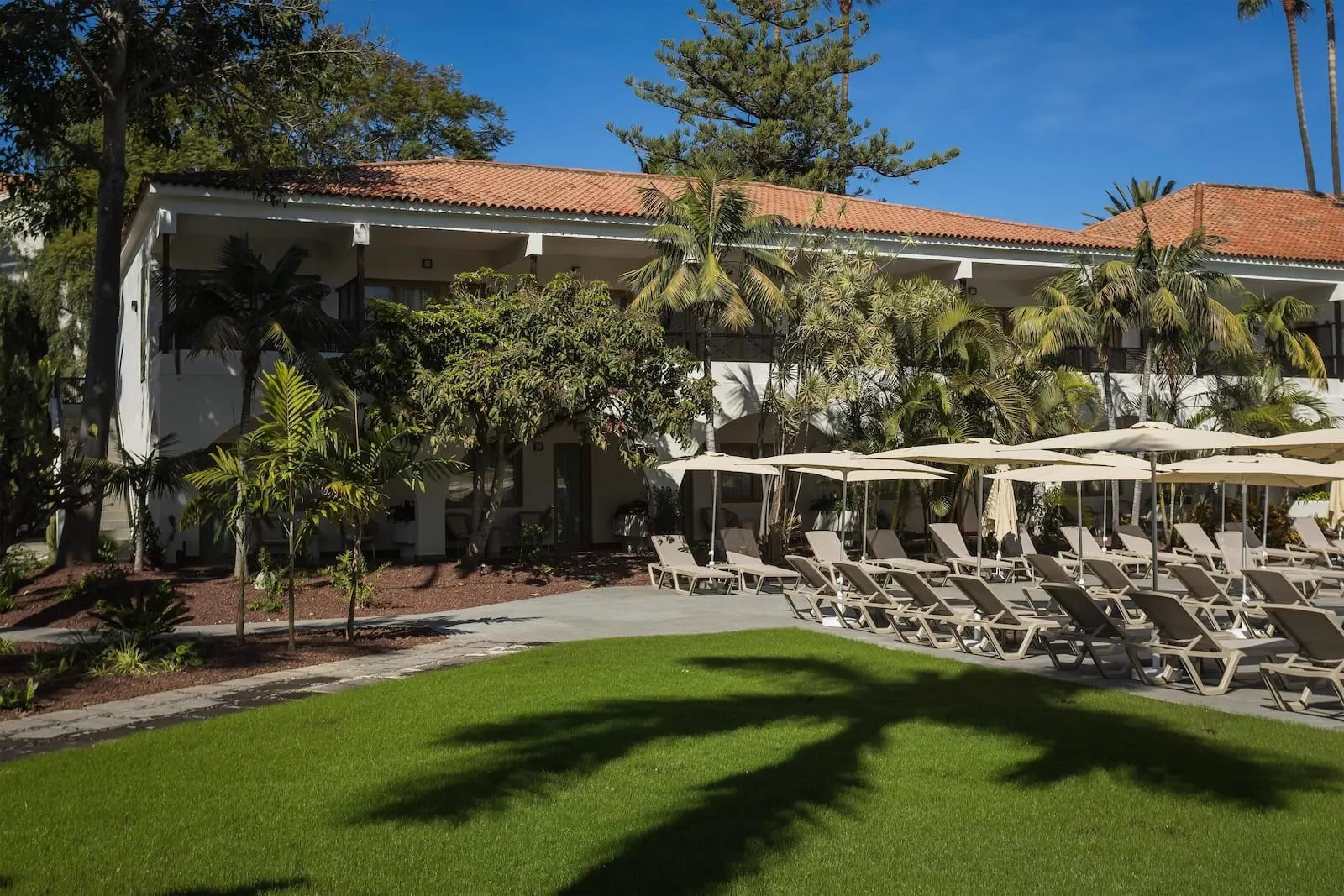 Radisson Resort & Residences Tenerife: A hotel with a tiled roof, outdoor lounge chairs, and palm trees