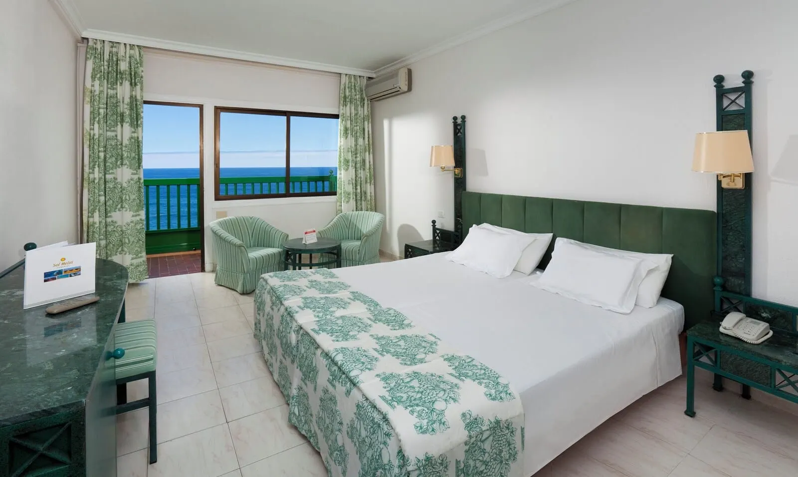 Sol Puerto de la Cruz Tenerife: A hotel room with a bed, a desk, a chair, a small table, a phone, and a view of the sea