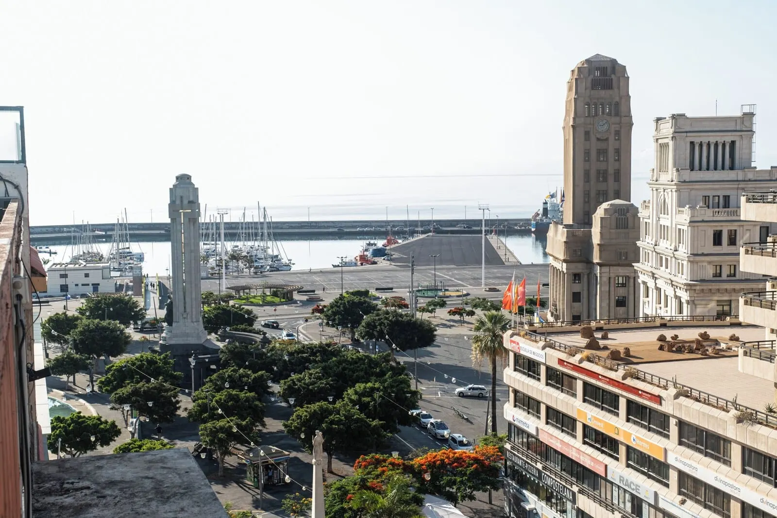 Hotel Adonis Plaza: A cityscape with a prominent monument, a tall building, and a marina with boats