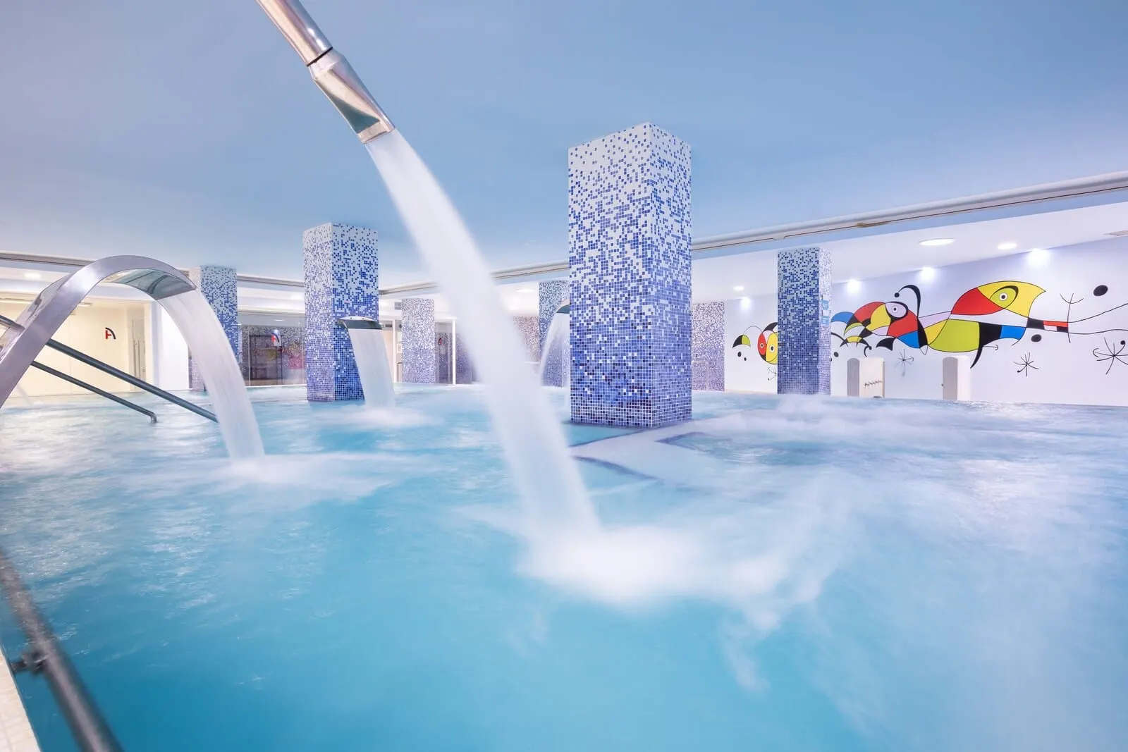 Alexandre Gala: A modern indoor pool with water jets, tiled walls, and colorful wall art