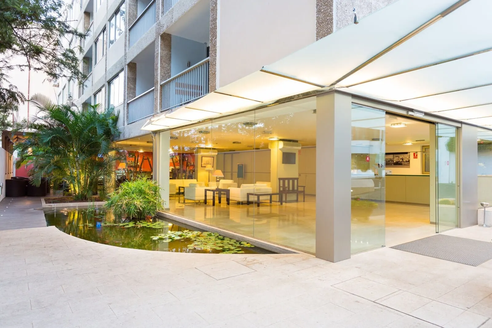 Hotel Colón Rambla: A hotel lobby with a glass entrance, a small indoor pond