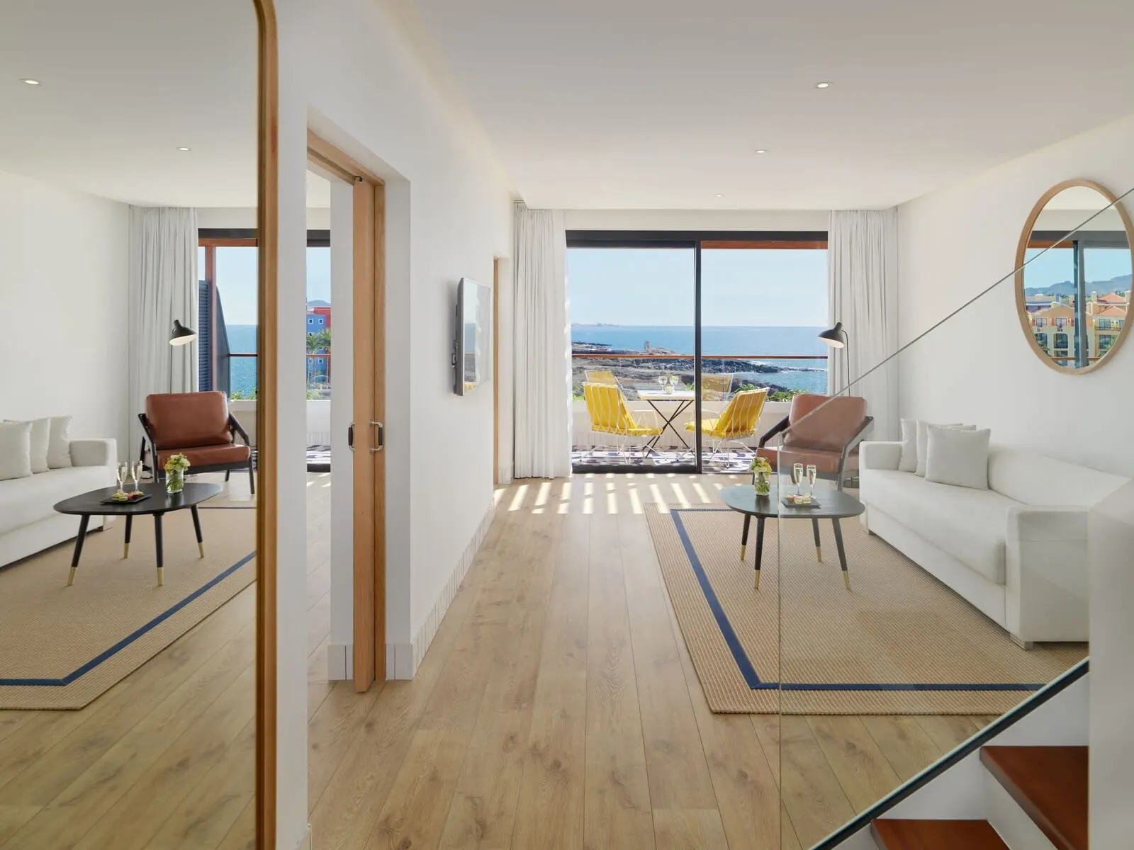 H10 Atlantic Sunset: A modern hotel room with a balcony, a white sofa, a brown armchair