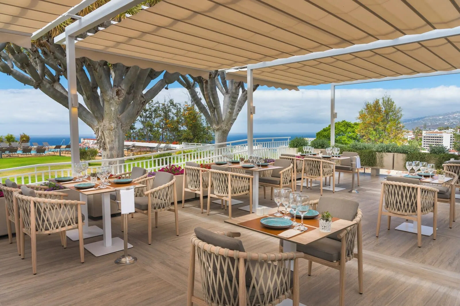 TUI BLUE Atlantic Hills: An outdoor dining area with tables and chairs, a large tree, and a view of the ocean