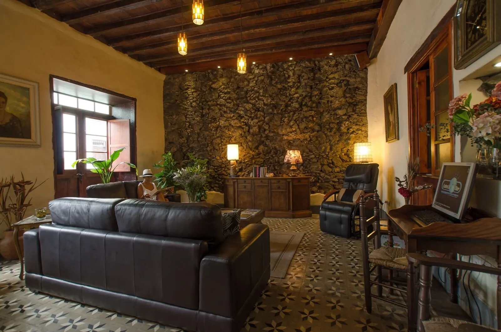 Garahotel: A cozy living room with a stone wall, leather sofa, wooden desk, and a laptop