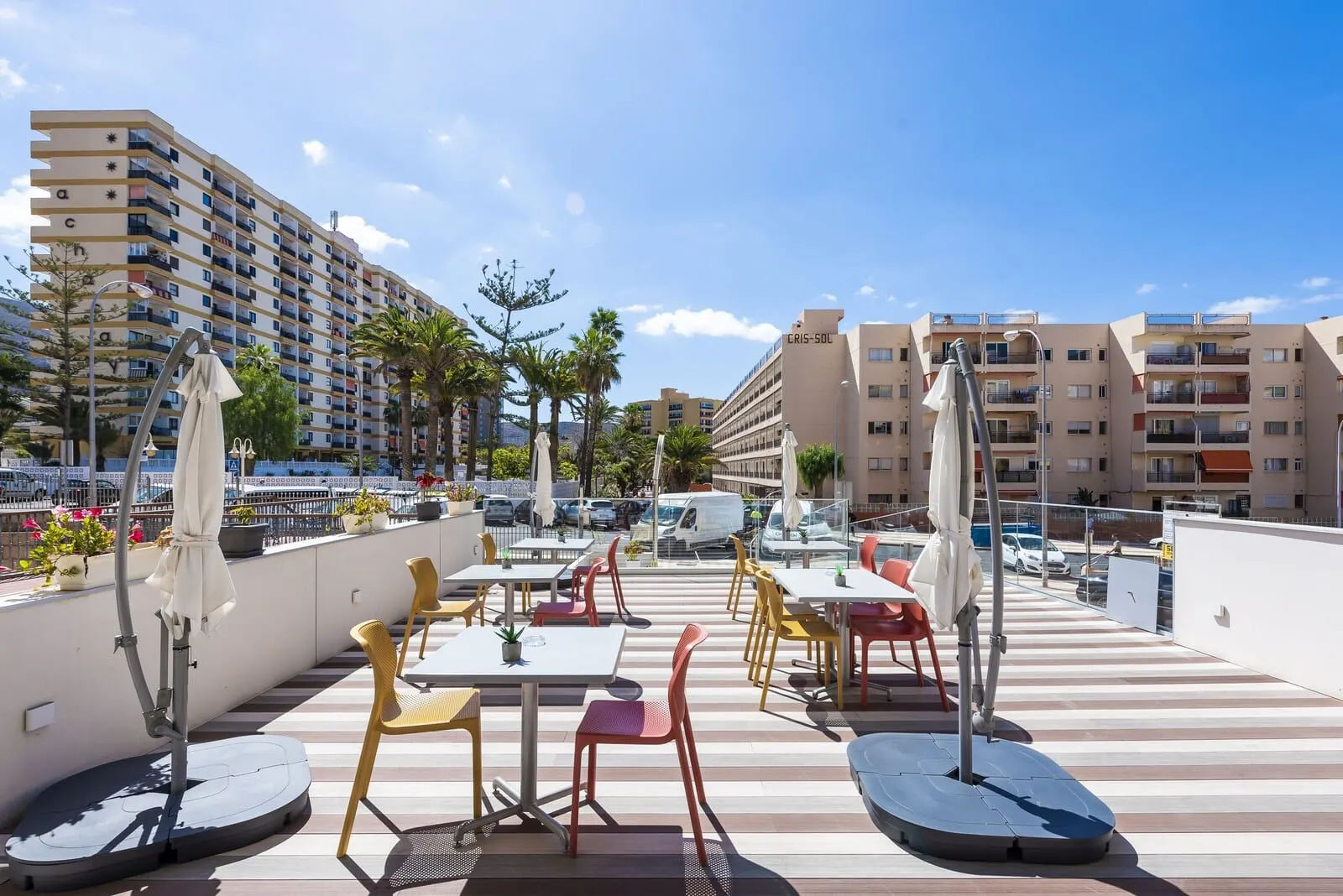 Andrea's Hotel Tenerife: An outdoor terrace with tables and chairs, umbrellas, and a pool area in the background