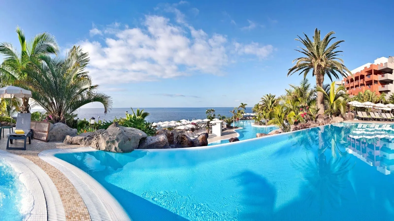 Roca Nivaria Gran Hotel: A resort pool with a view of the ocean, surrounded by palm trees and lounge chairs