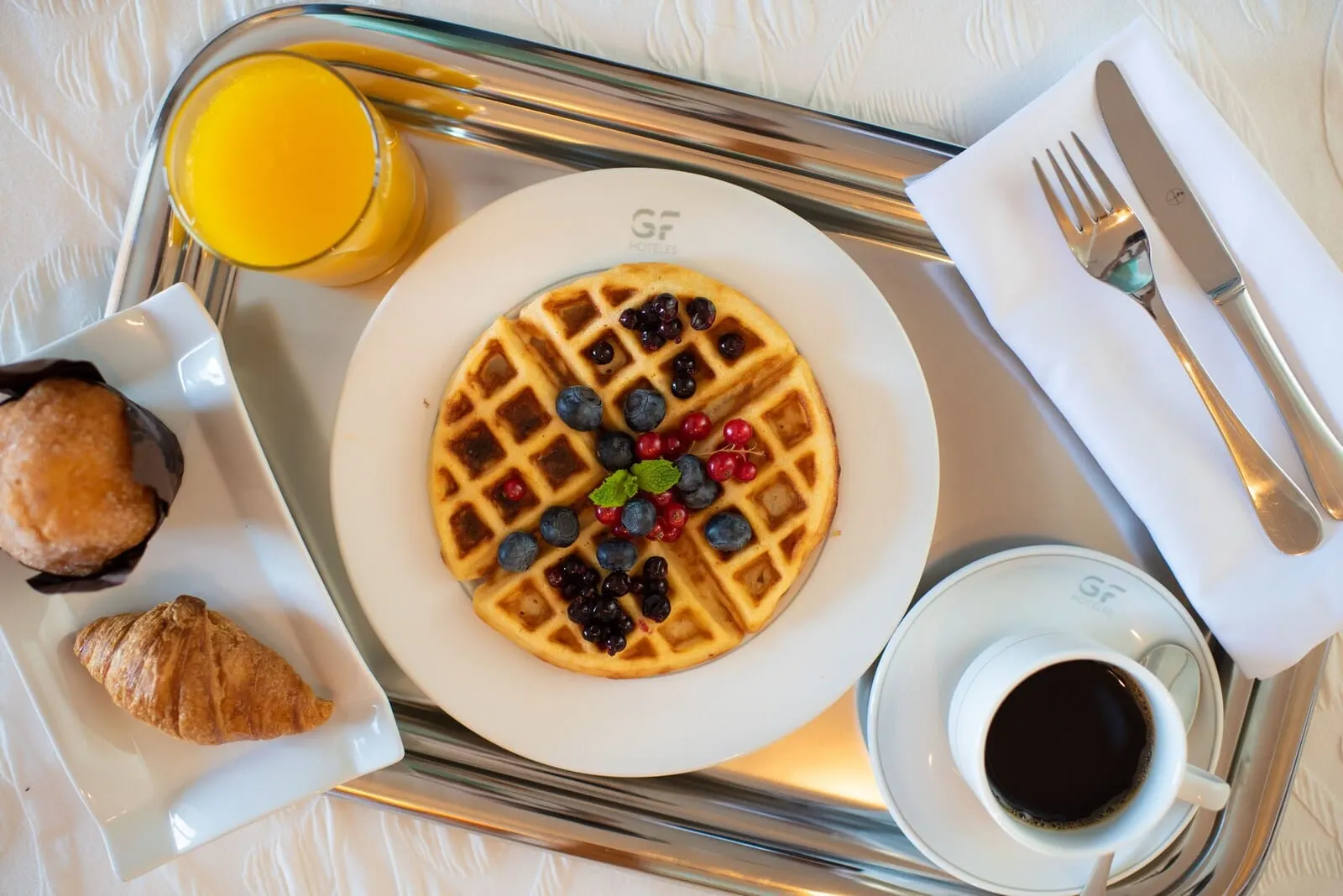 GF Gran Costa Adeje: A breakfast tray with a waffle, croissant, and juice