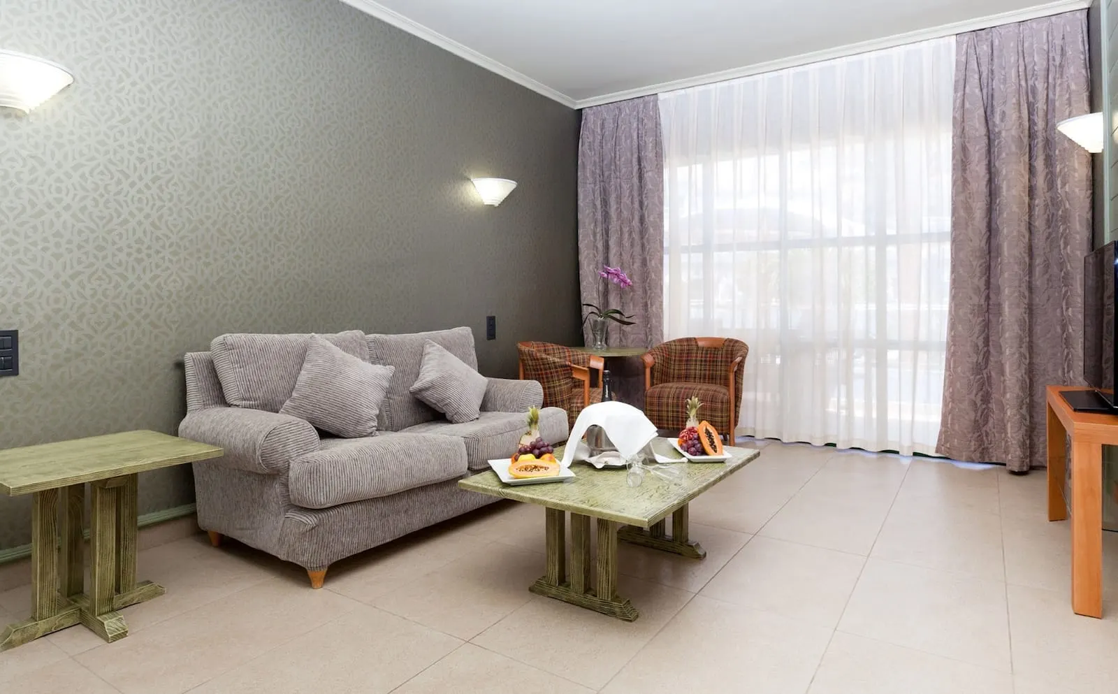 Hotel Colón Guanahaní: A living room with a grey sofa, two small tables, a wicker chair