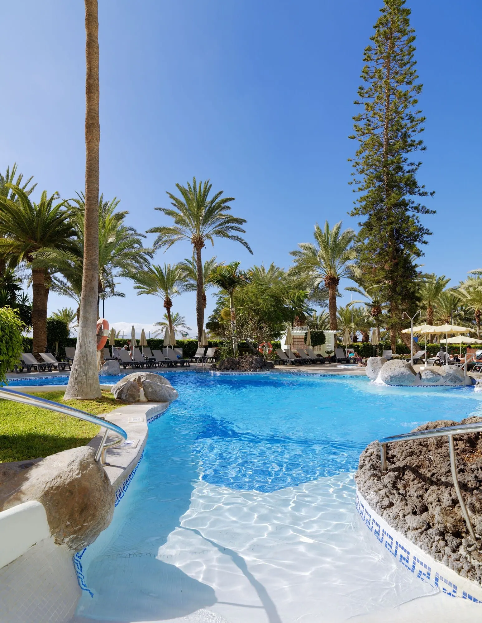 H10 Big Sur: A clear blue pool surrounded by palm trees and lounge chairs