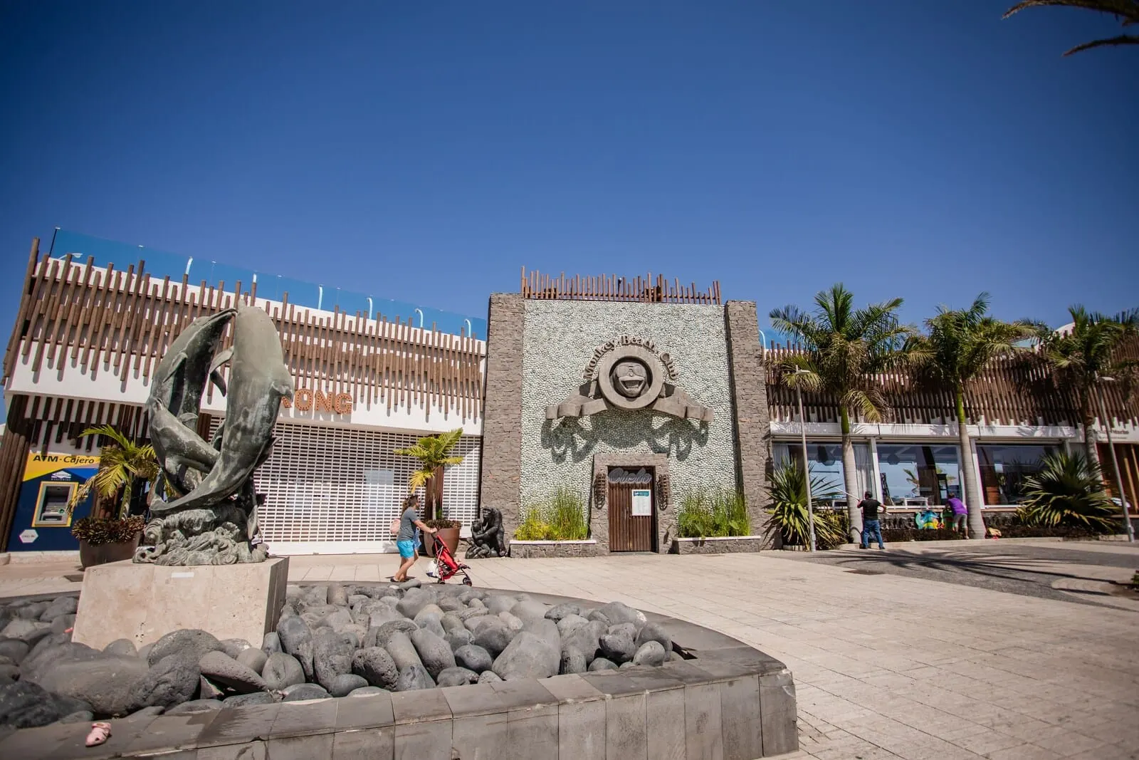 Servatur Caribe: A plaza with a stone sculpture, a building with a mural, and palm trees