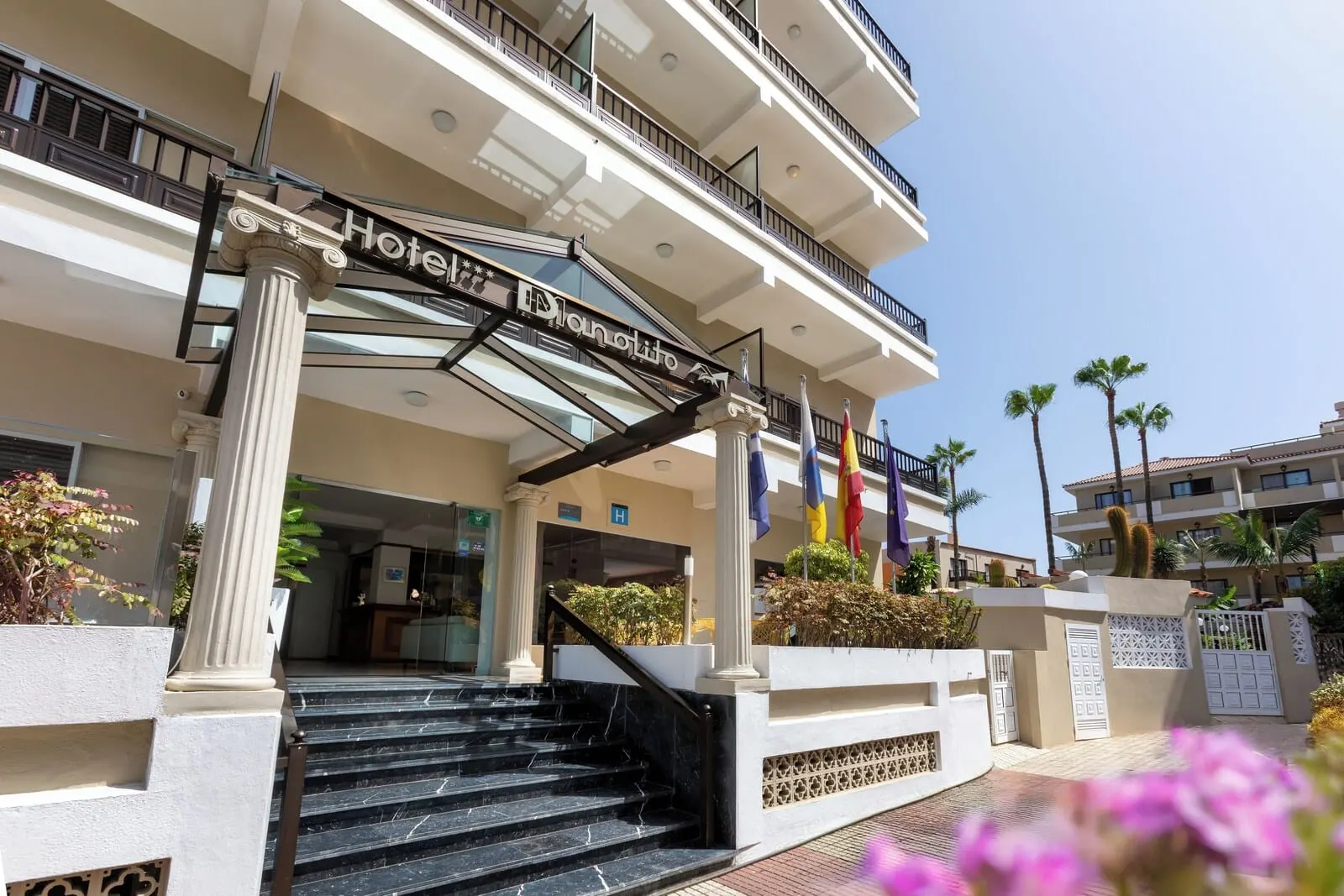 Hotel Don Manolito: A hotel entrance with a grand staircase, a glass canopy, and multiple balconies