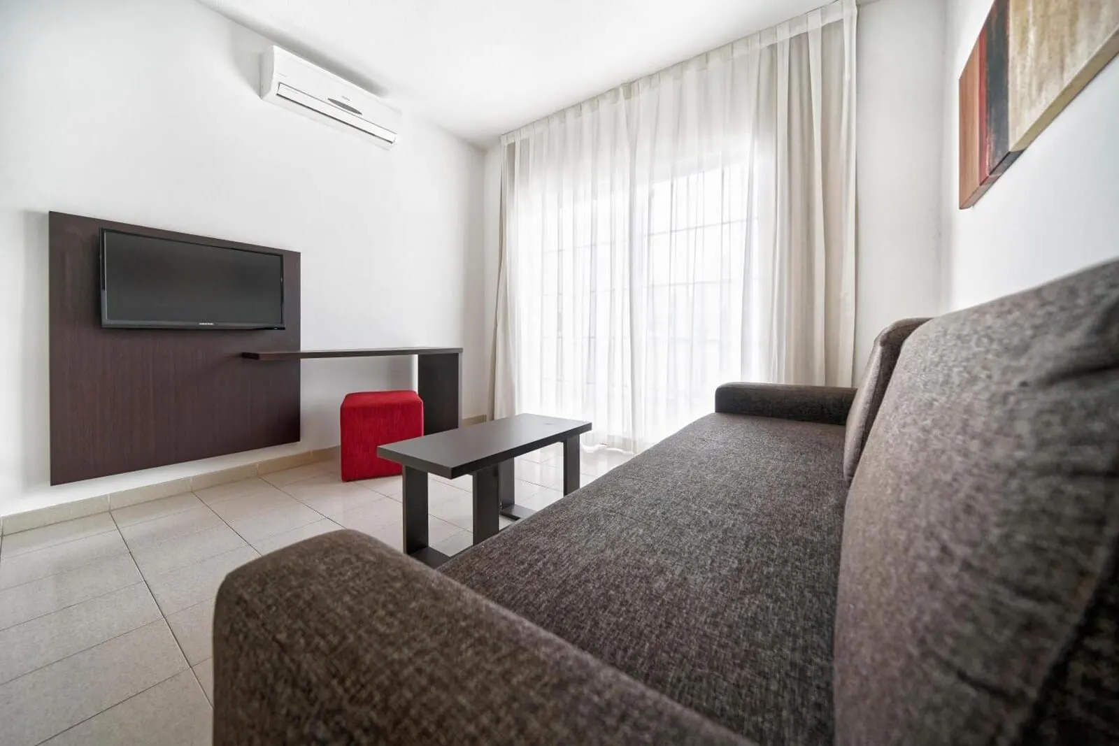 BLUESEA Bahía Fañabé Villas: A modern living room with a flat-screen TV mounted on the wall, a grey sofa