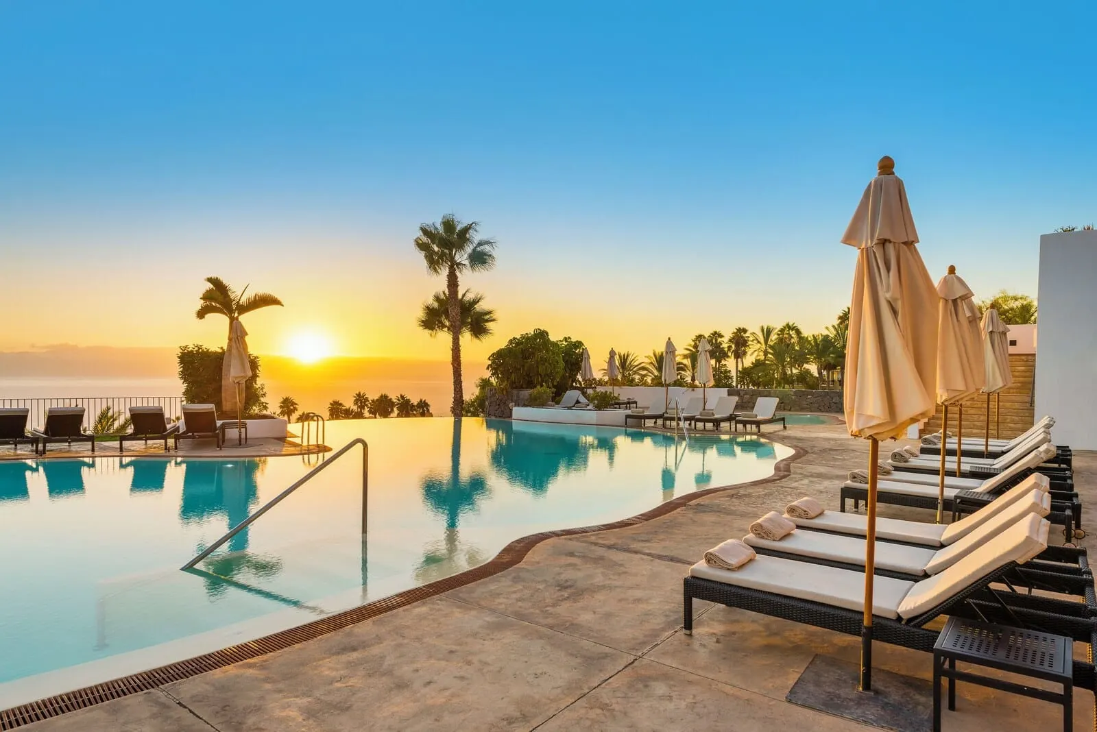 Las Terrazas de Abama Suites: A poolside area with lounge chairs and umbrellas, a clear sky, and a sunset