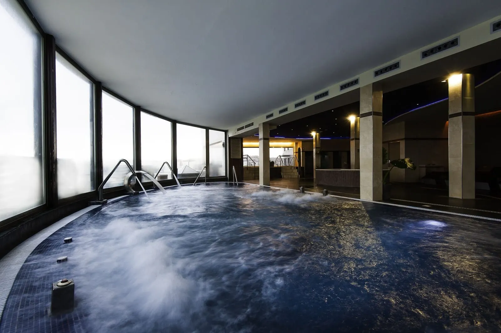 KN Hotel Arenas del Mar: A large indoor hot tub with a view of the city skyline through large windows
