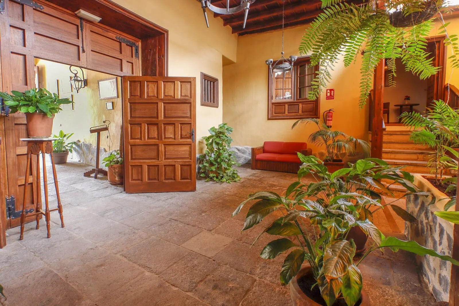 Hotel Rural Bentor: A spacious interior with a large wooden door, multiple potted plants, and a red sofa
