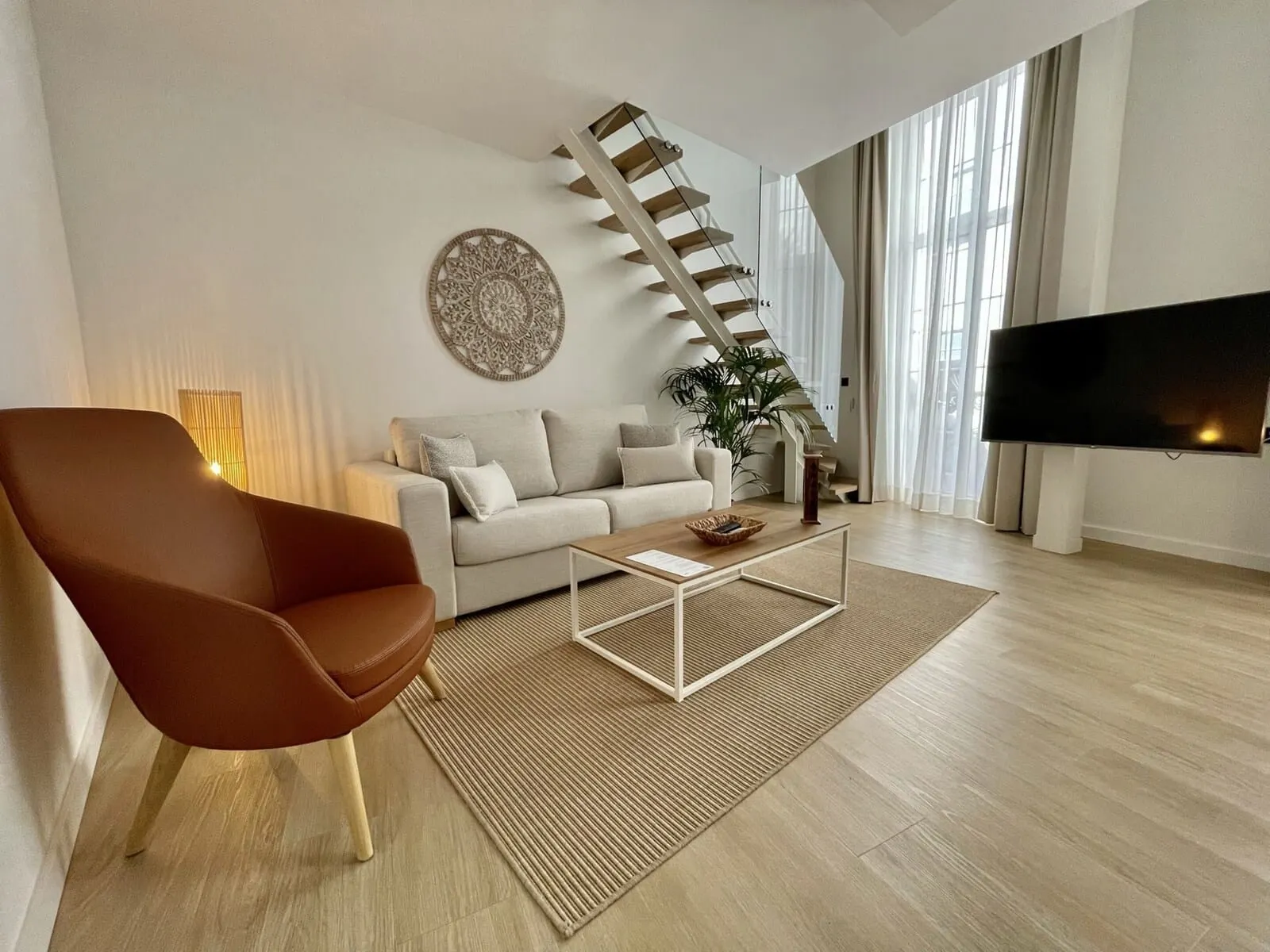 Hi Suites: A modern living room with a sofa, a coffee table, a TV, and a staircase