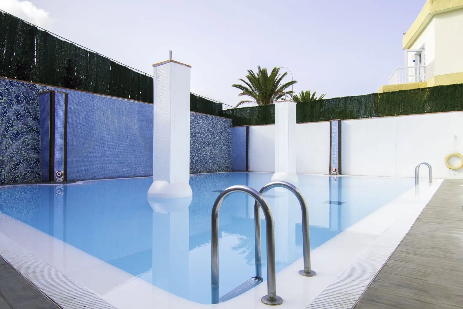 Checkin Bungalows Atlántida: A swimming pool with metal railings, a tiled wall, and a palm tree