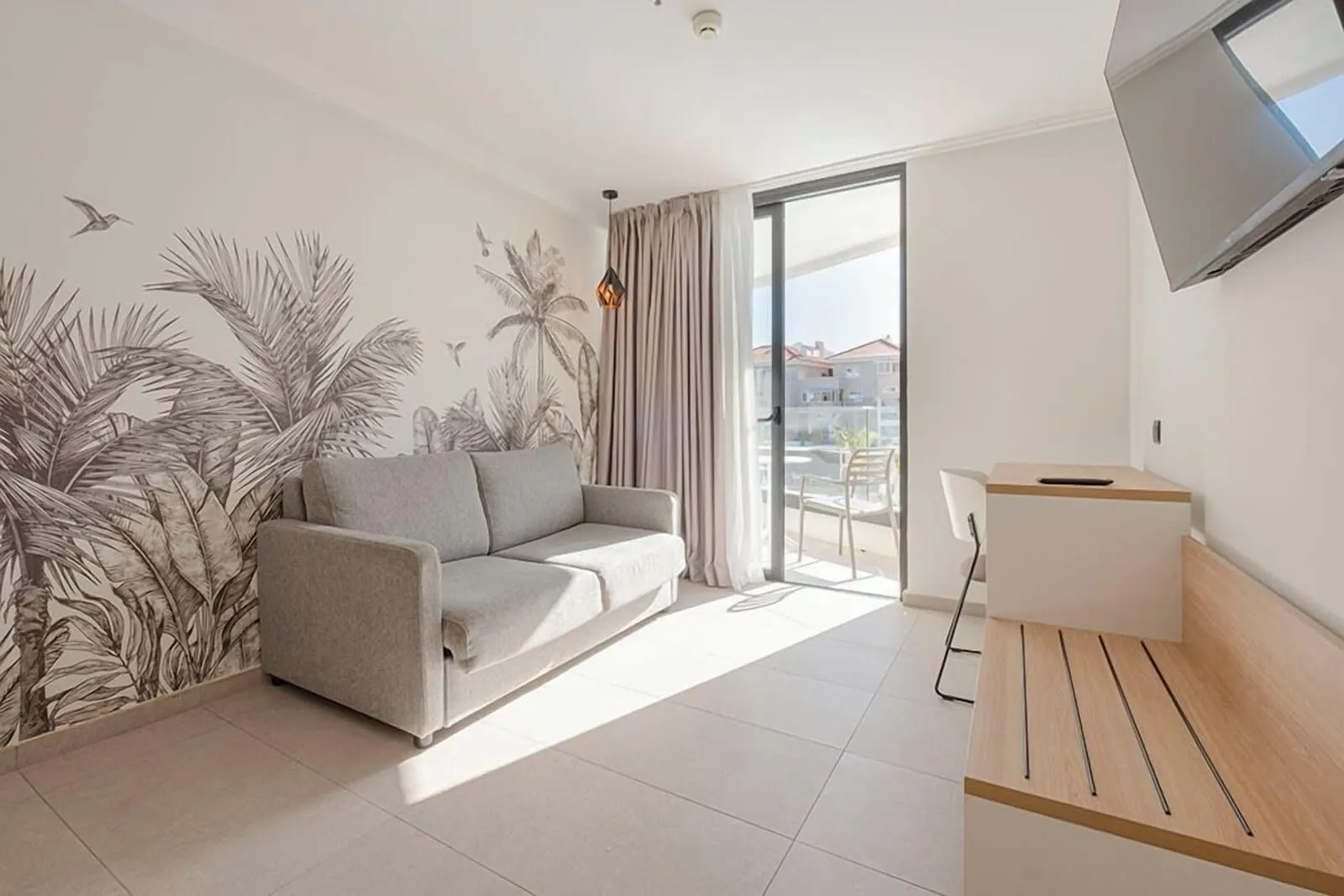 MYND Adeje: A modern living room with a sofa, a small desk, and a large window with curtains