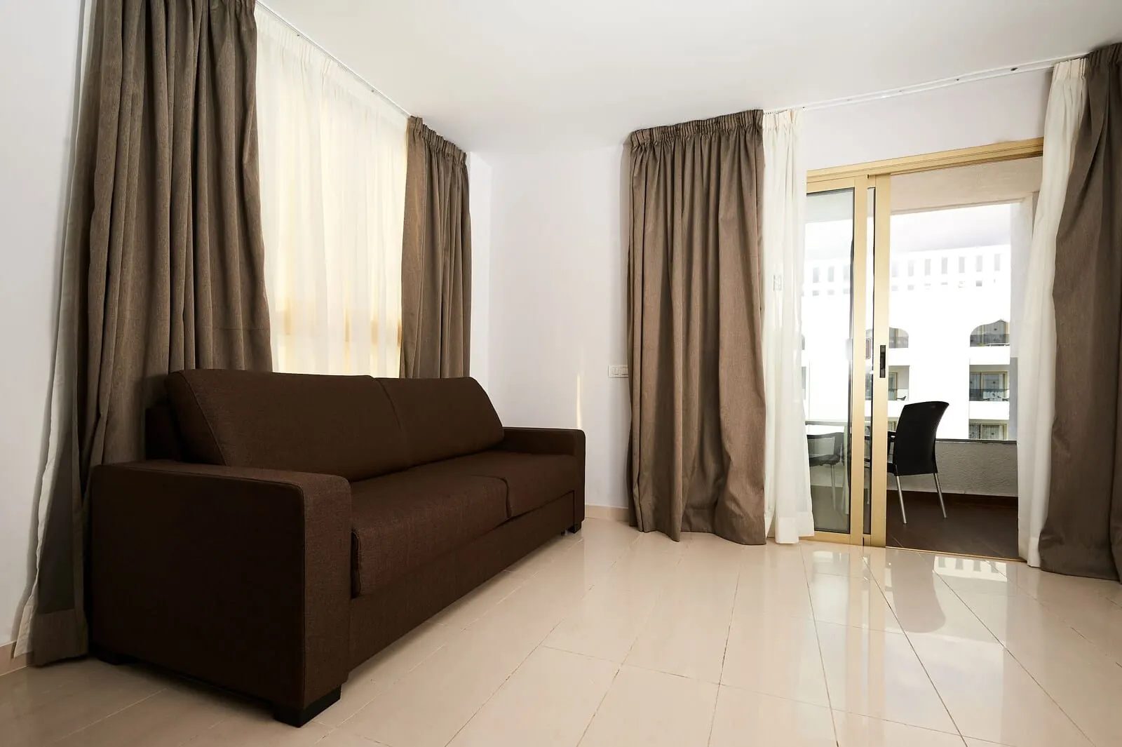 KN Aparthotel Columbus: A modern living room with a brown sofa, large windows with sheer curtains