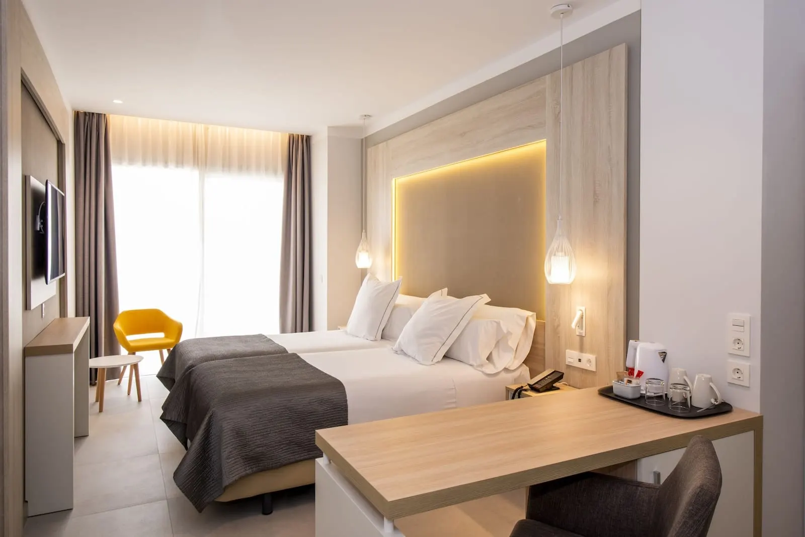Bahia Principe Explore Fantasia: A modern hotel room with two beds, a desk, a chair, a TV, and a window with curtains