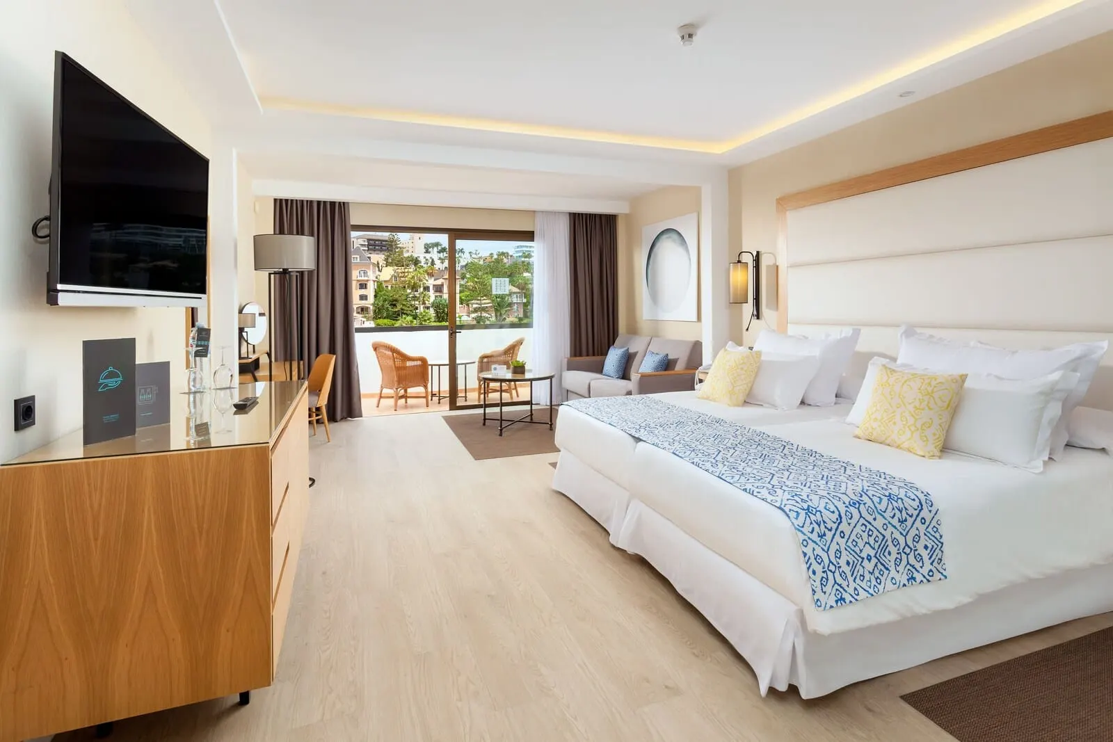 Gran Tacande Wellness & Relax: A hotel room with a large bed, a desk, a TV, and a balcony with a view of buildings