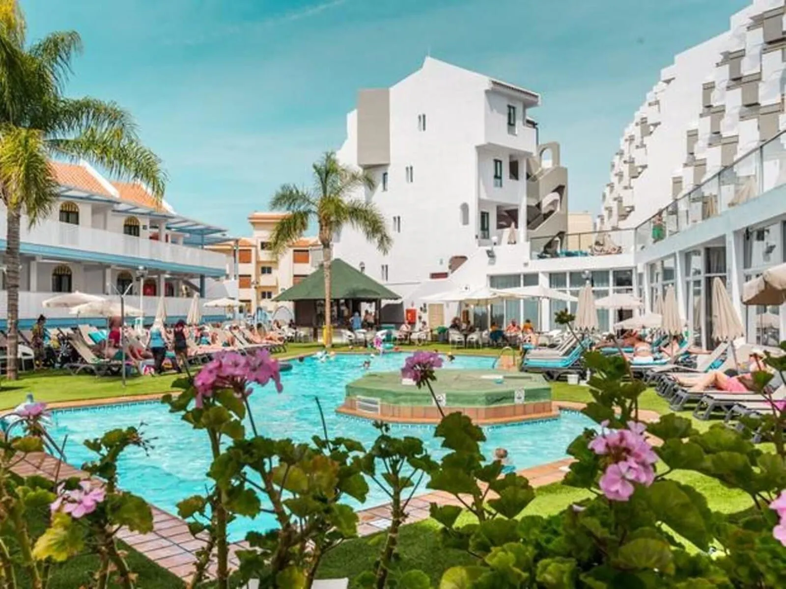 Playaolid Suites & Apartments: A pool area with lounge chairs, palm trees, and a building with balconies