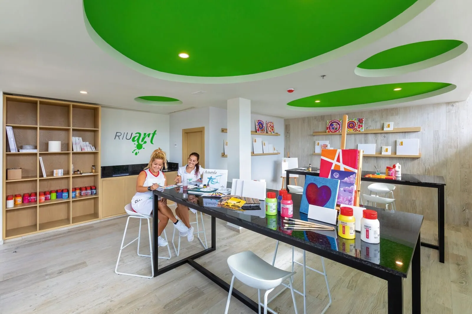 Hotel Riu Buenavista: A modern art studio with a glass table, stools, and art supplies