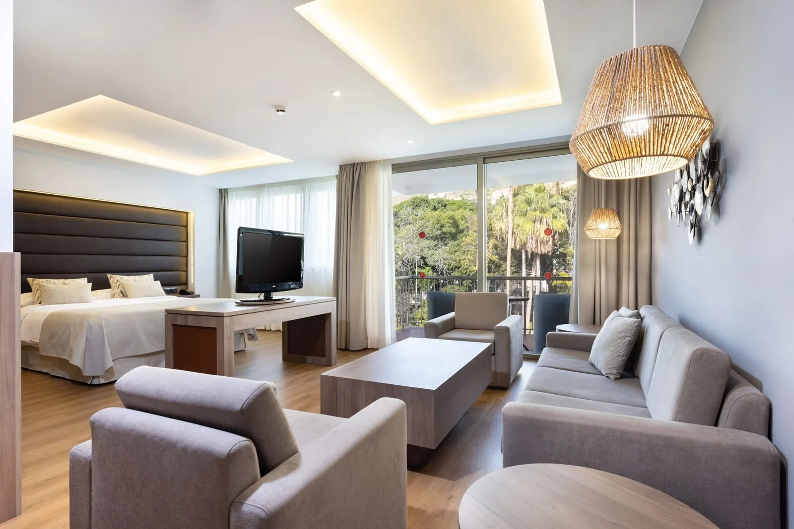 Hotel Colón Rambla: A modern hotel room with a bed, sofa, TV, and a balcony with a view