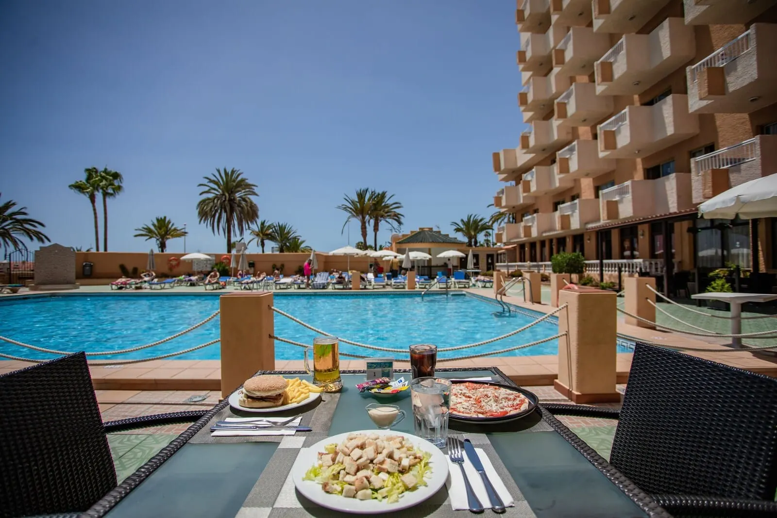 Servatur Caribe: A poolside dining area with a view of the pool, lounge chairs, and palm trees