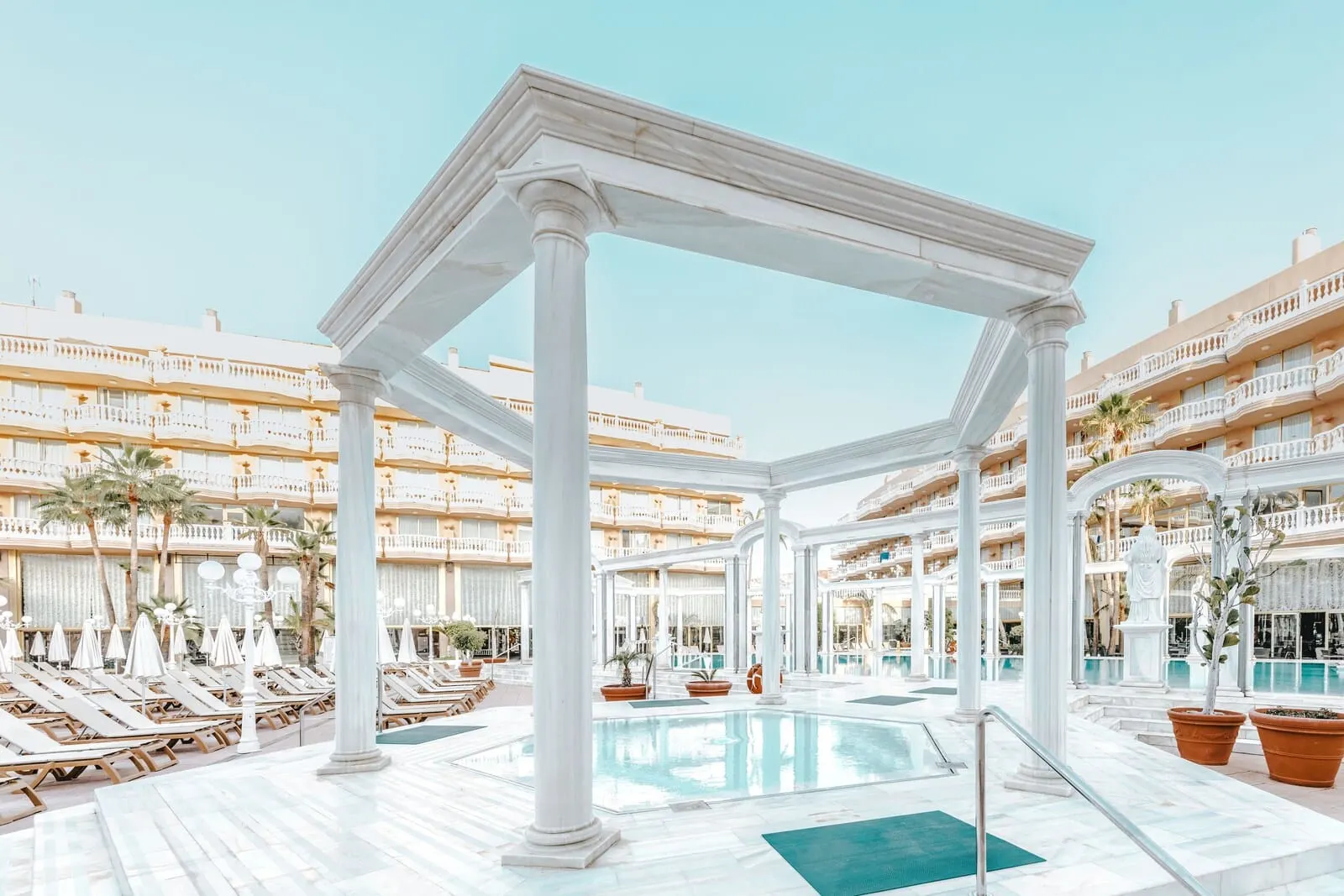 Cleopatra Palace: A hotel pool area with white columns, sun loungers, and a clear blue pool