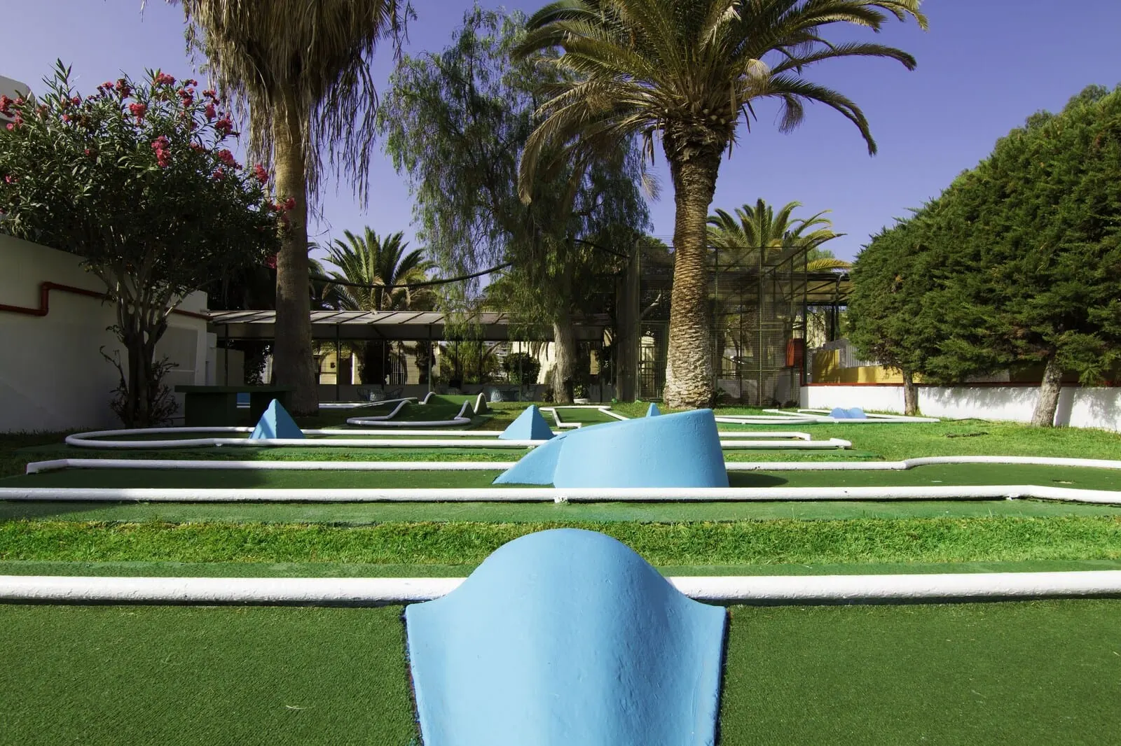 Checkin Bungalows Atlántida: A landscaped garden with palm trees, a clear blue sky, and geometric sculptures