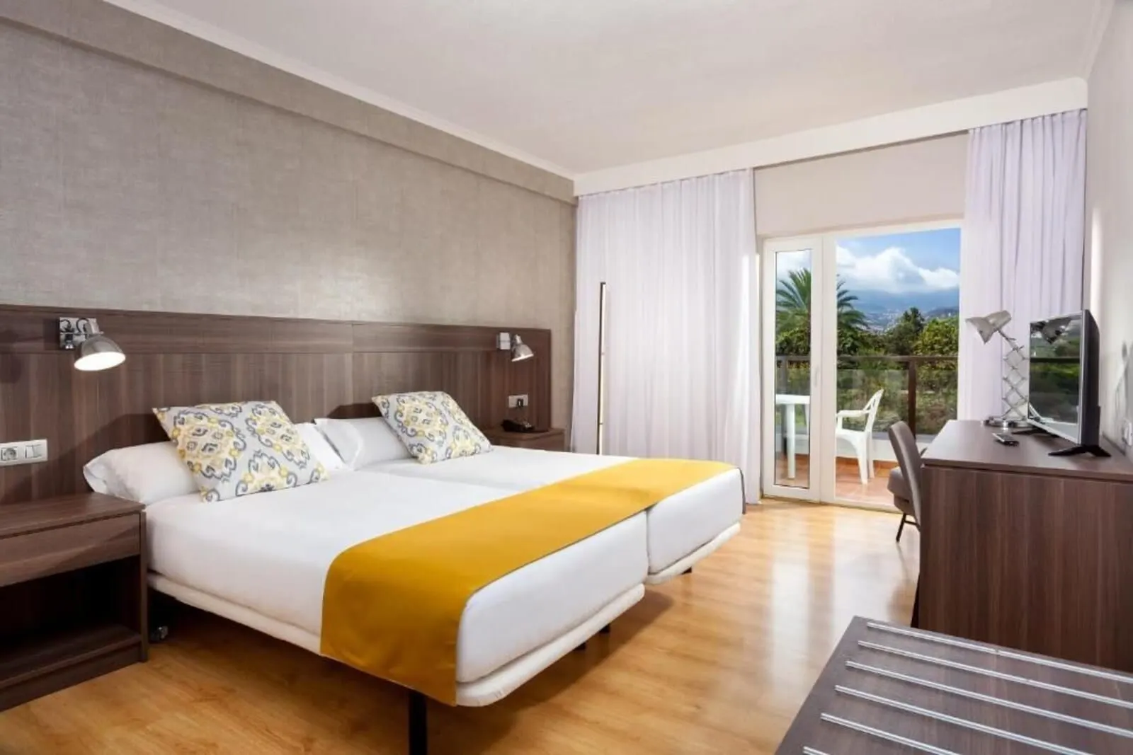 Hotel TRH Taoro Garden: A hotel room with a bed, bedside lamps, a desk, and a view of the outdoors