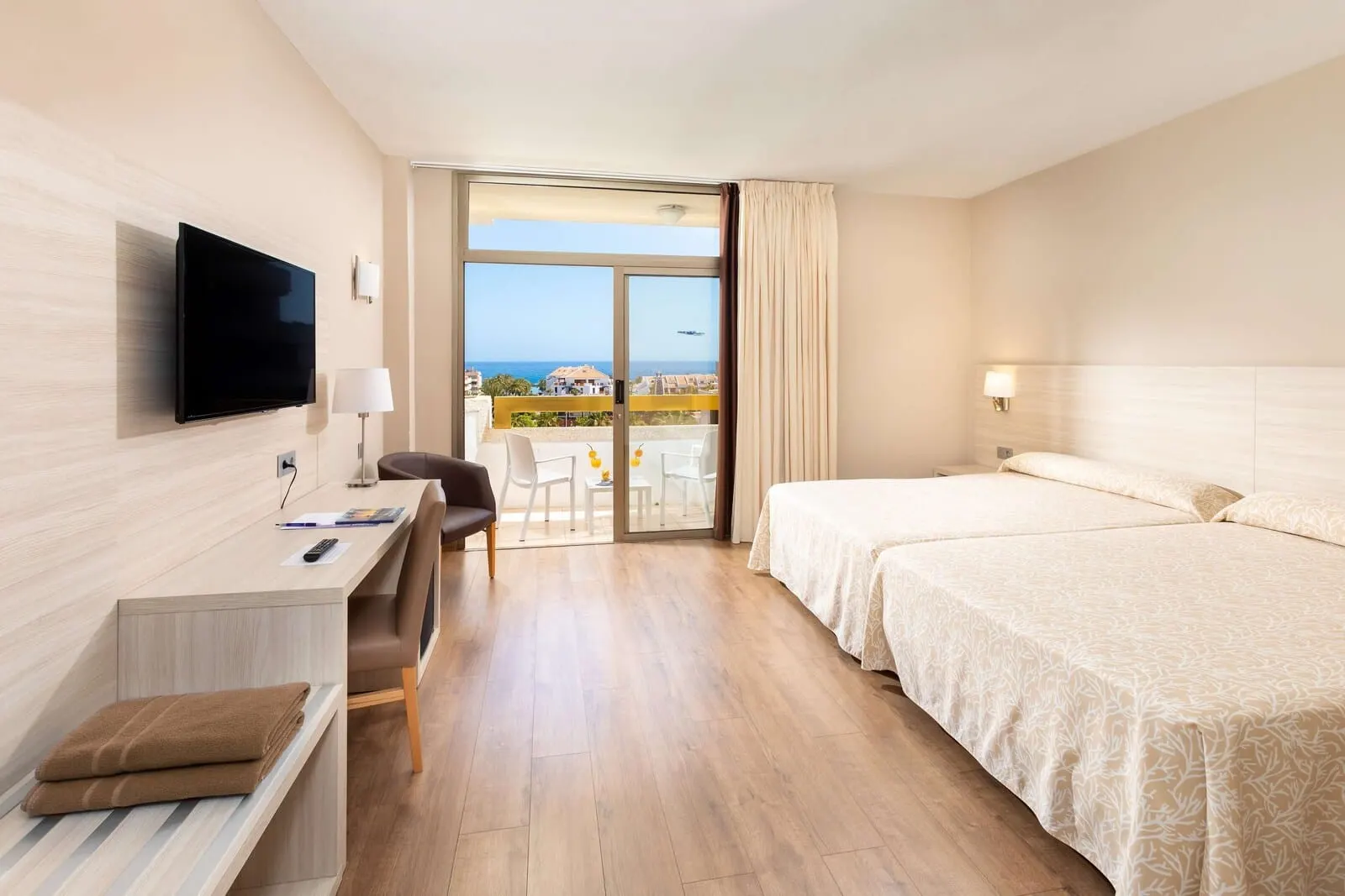 Best Tenerife: A hotel room with a desk, two beds, a TV, and a balcony with a view