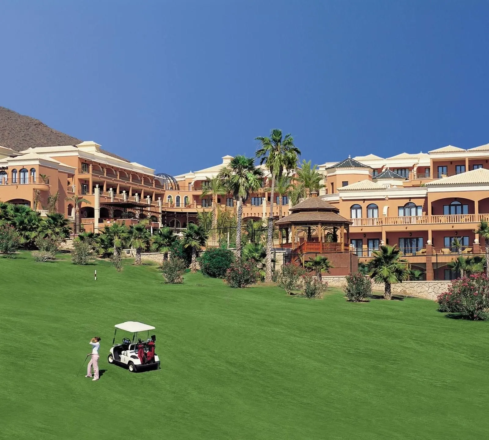 1881 Tenerife Madrigueras Golf Hotel: A golf course with a clubhouse and a building with multiple balconies and a gazebo