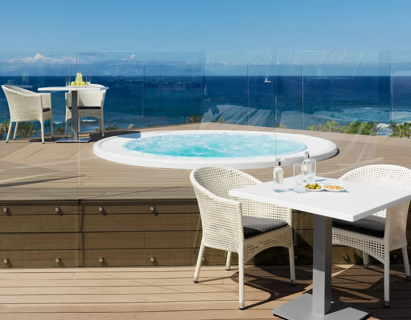 H10 Conquistador: A deck with a hot tub, white wicker chairs, a table with drinks
