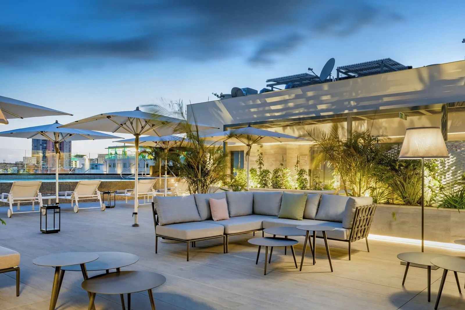 AC Hotel Tenerife: An outdoor seating area with a sofa, round tables, and umbrellas