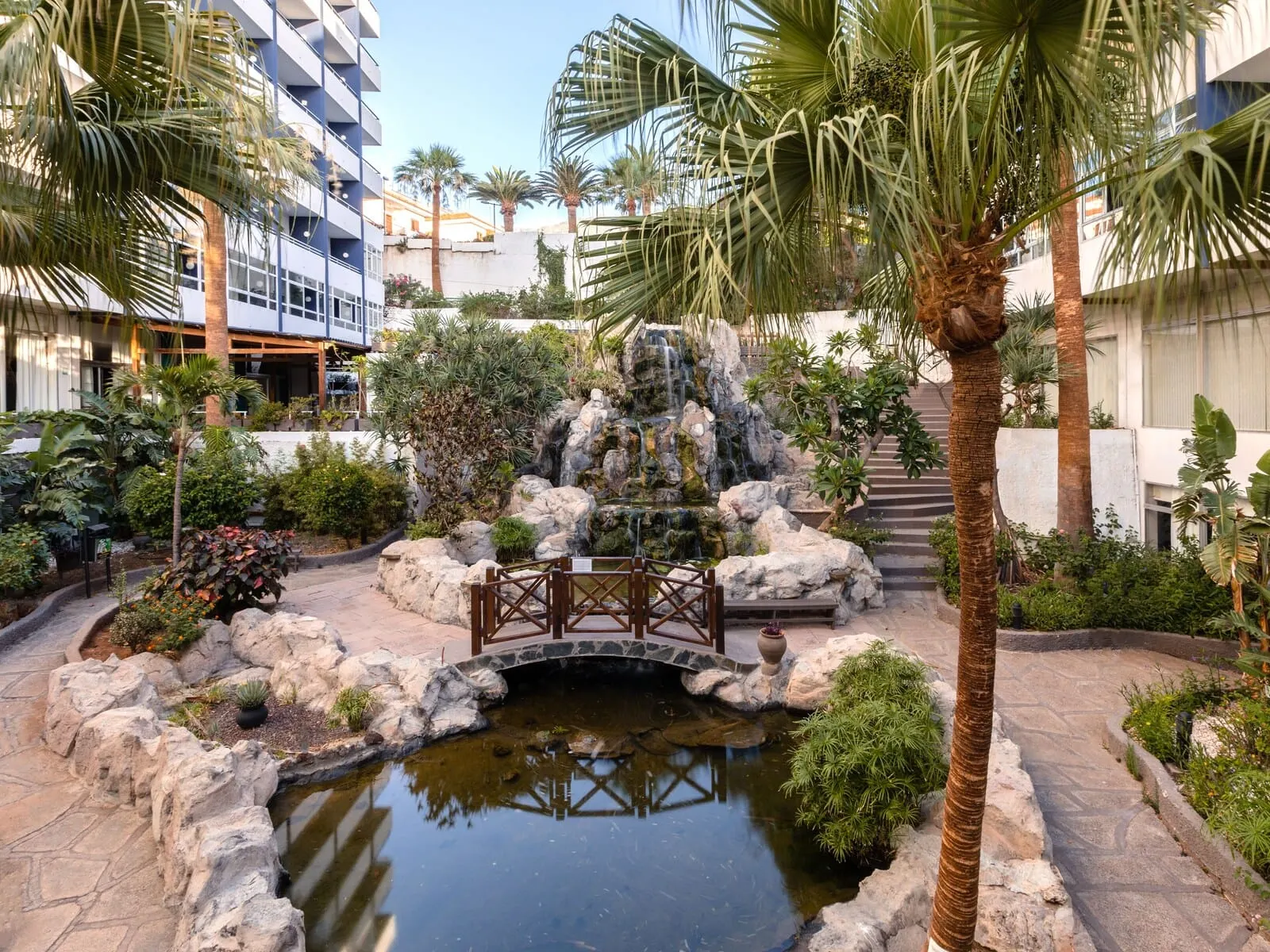 Catalonia Punta del Rey: A landscaped courtyard with a small pond, palm trees, and a waterfall
