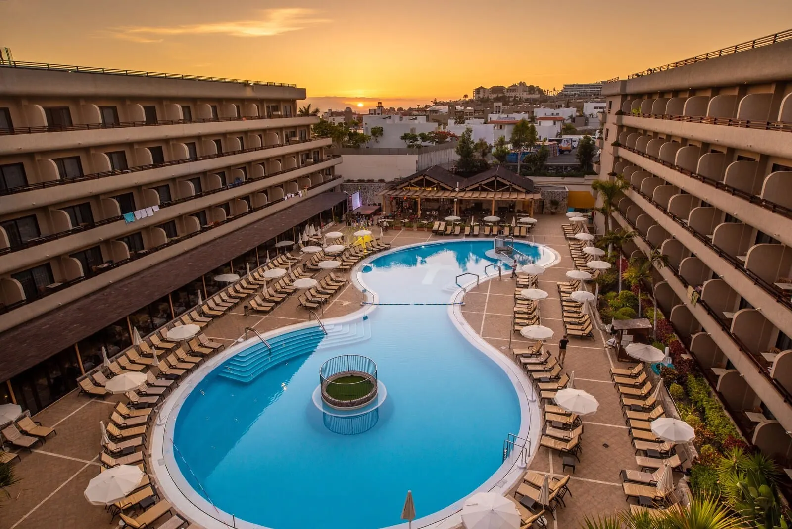 GF Fañabé: A hotel pool area with multiple levels of balconies, sun loungers, and a central pool