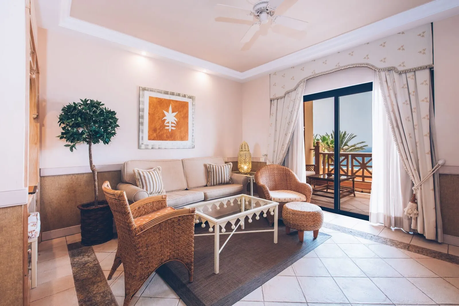 JOIA El Mirador by Iberostar: A living room with a sofa, two wicker chairs, a glass coffee table, a potted plant