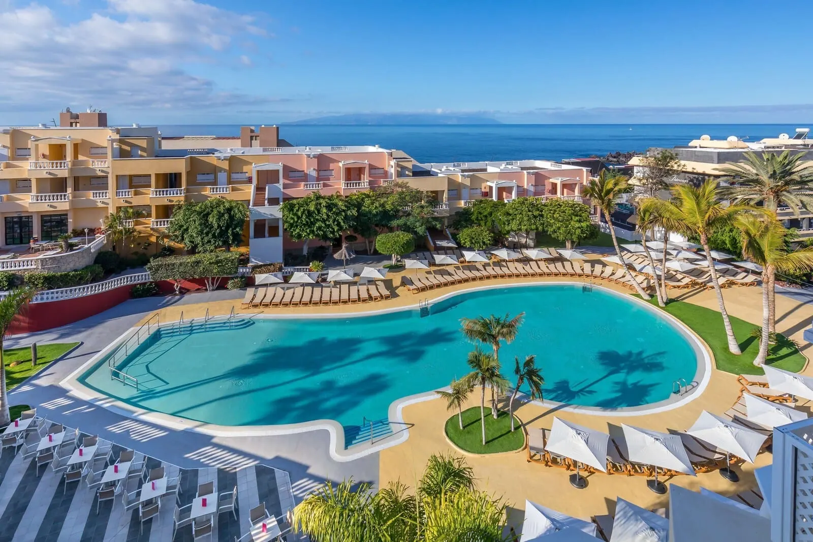 Servatur Isora Suites: A resort with a large pool, sun loungers, and a view of the sea