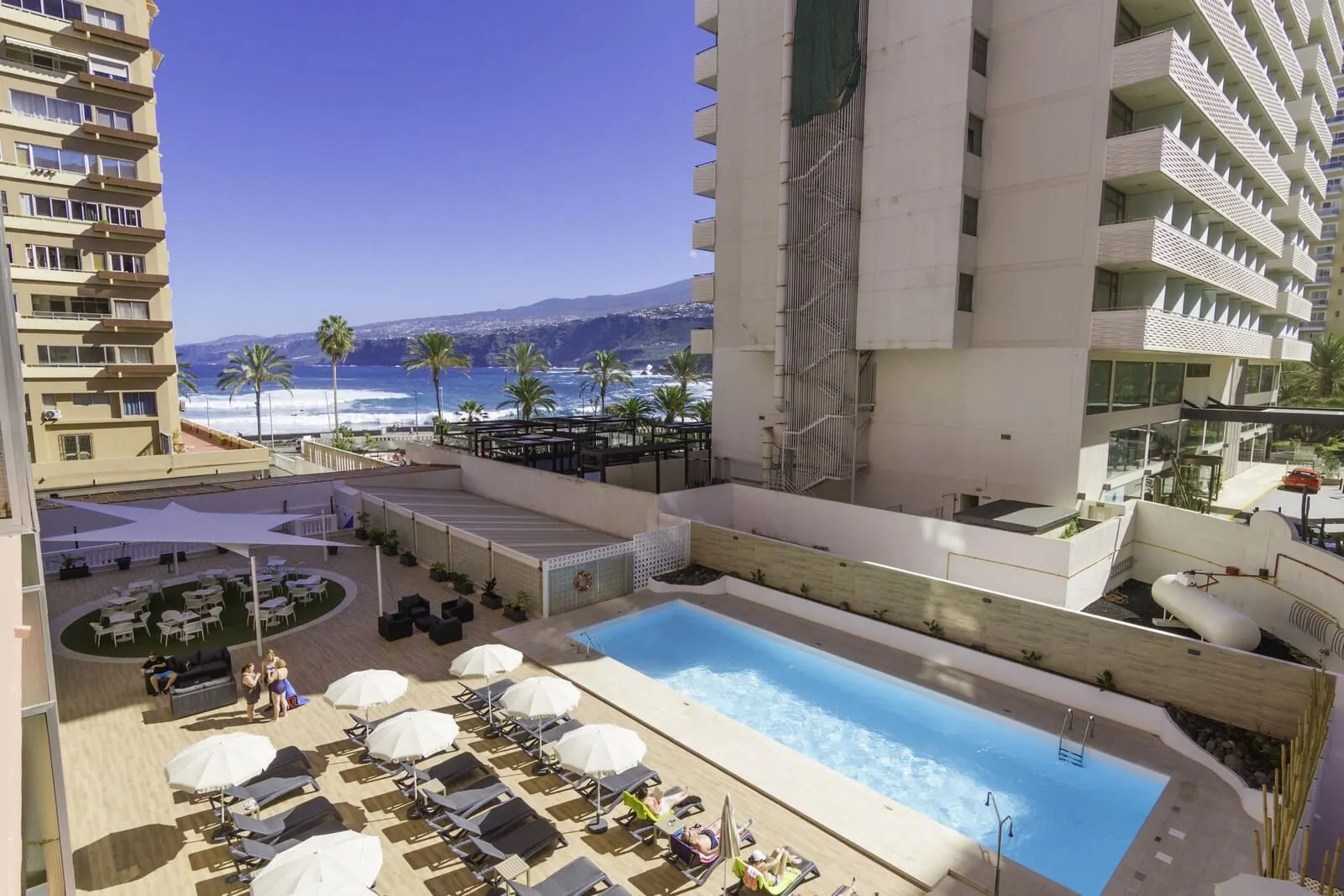 Checkin Concordia Playa: A rooftop pool area with lounge chairs and umbrellas, overlooking a beach and ocean