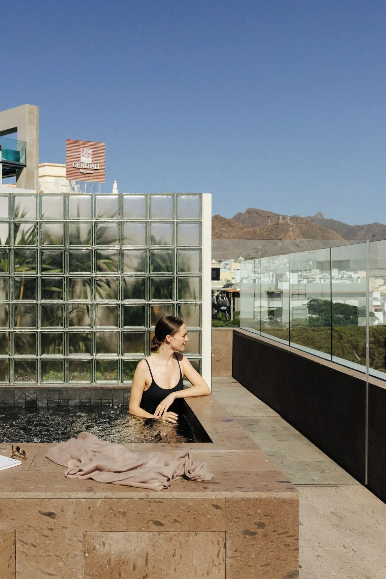 Hotel Taro Santa Cruz: A woman sitting by a reflective pool with a cityscape and mountains in the background