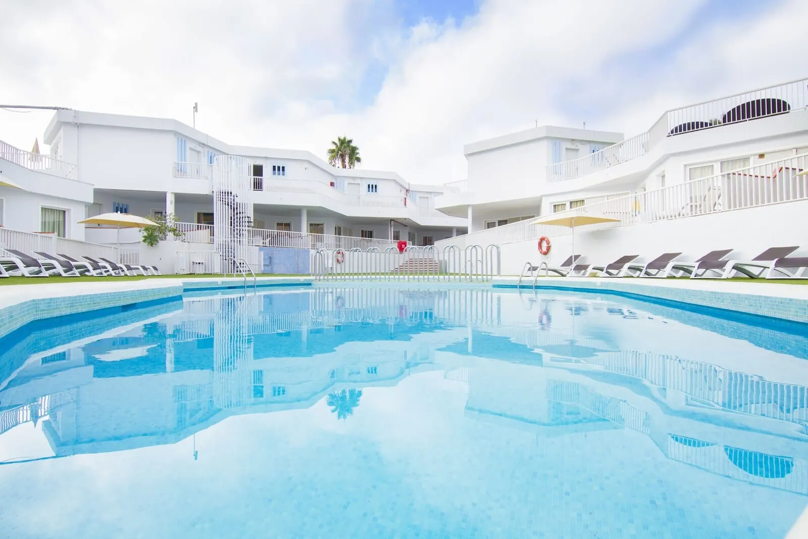 Checkin Bungalows Atlántida: A swimming pool surrounded by white buildings with balconies, a palm tree