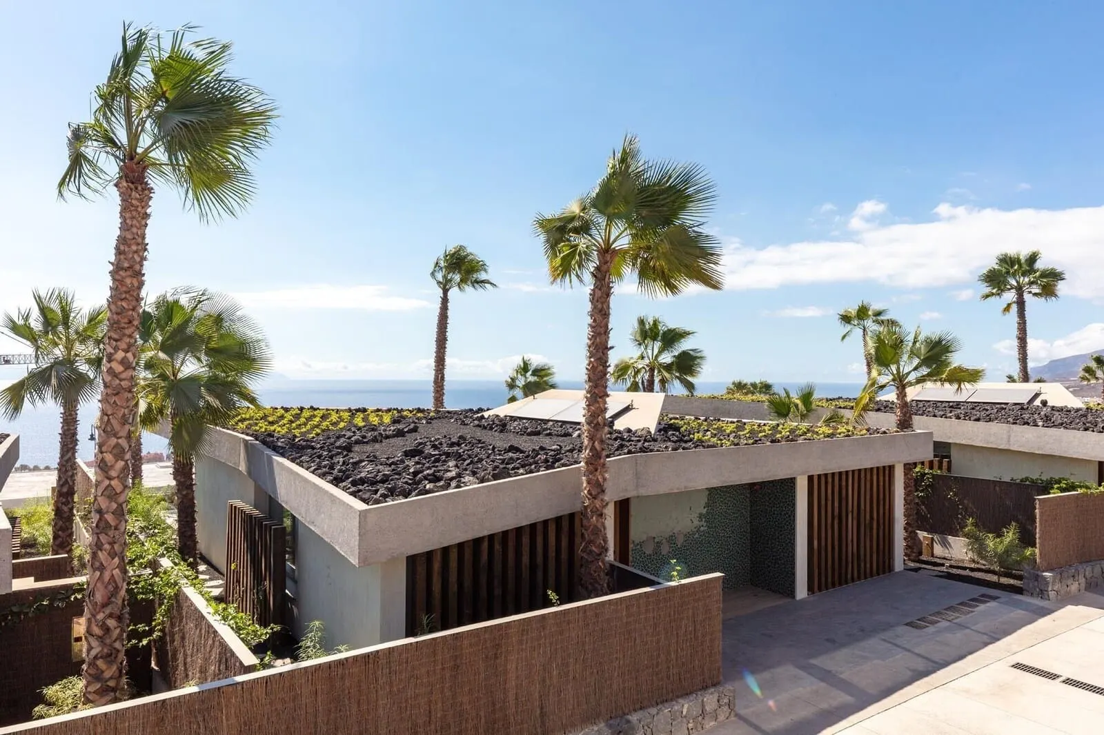 Los Jardines de Abama Suites & Villas: A modern building with a rooftop garden, palm trees, and a view of the ocean