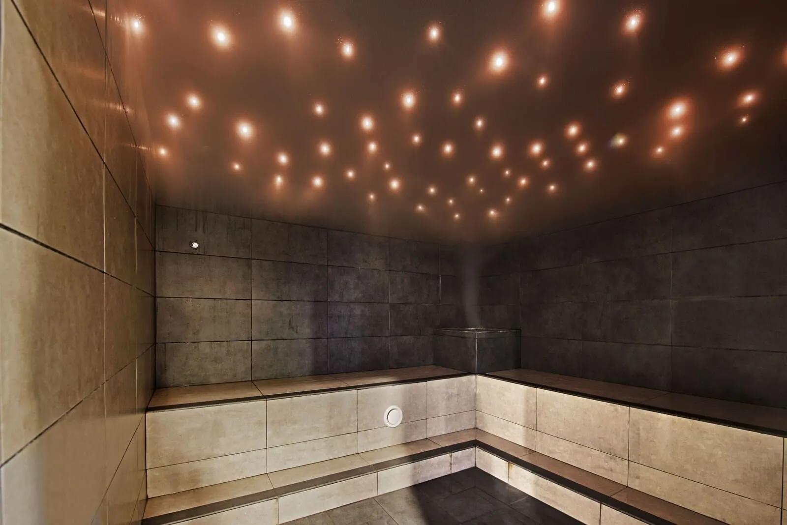 KN Aparthotel Columbus: A modern, dimly lit sauna with a tiled floor and walls