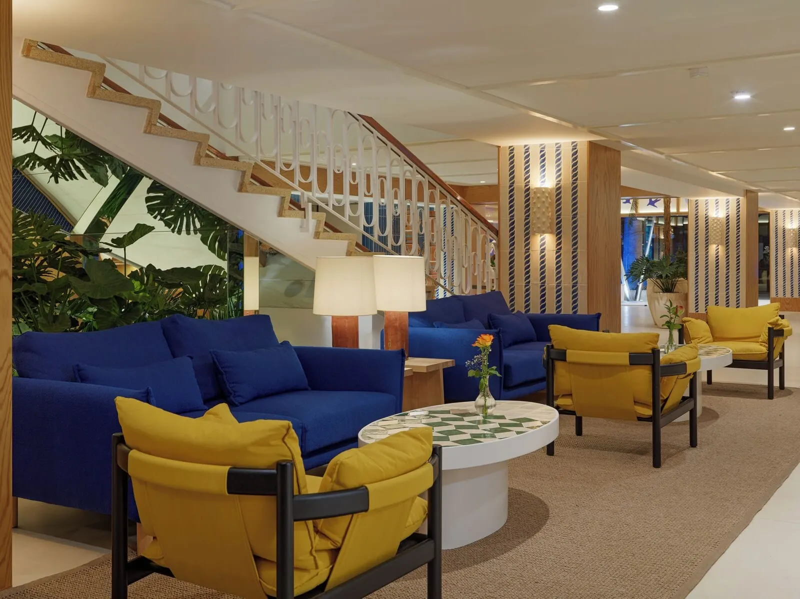 H10 Tenerife Playa: A modern lobby with blue sofas, yellow chairs, a staircase, and a large plant