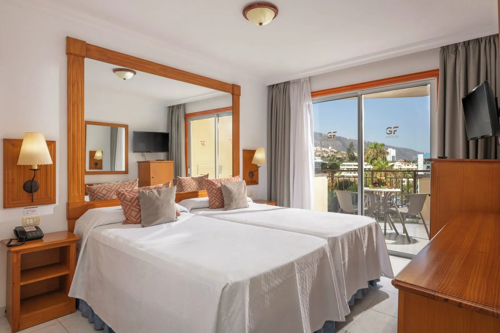 GF Noelia: A hotel room with two beds, a balcony with a table and chairs, a TV