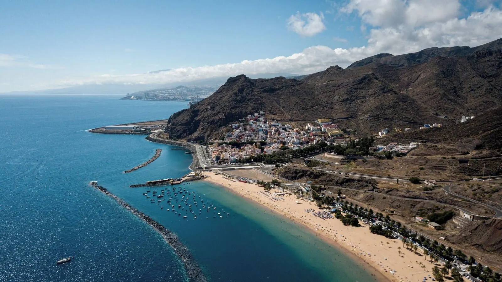 Hotel Adonis Capital: A coastal town with a beach, boats, and a mountainous backdrop